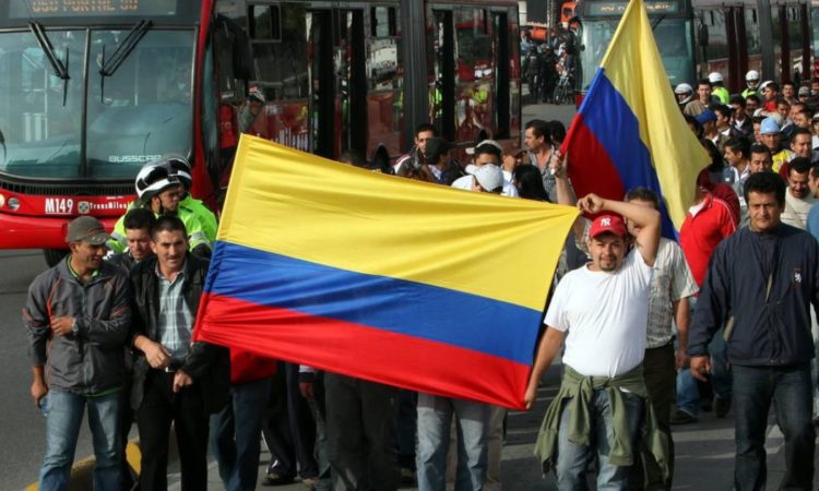 Trabajadores del transporte en Bogotá marchando con banderas de Colombia al lado del Transmilenio
