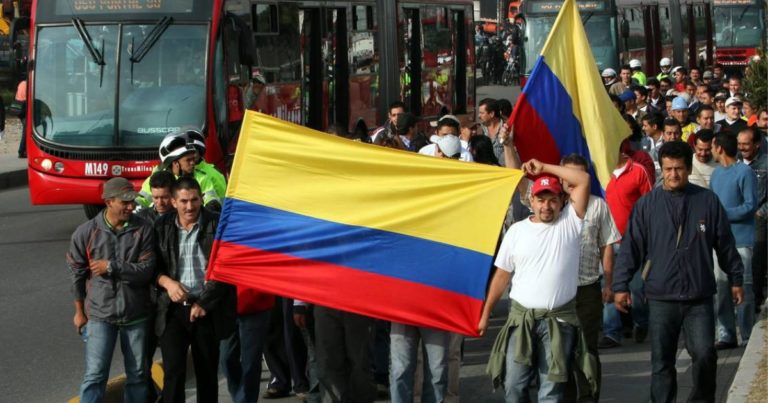 Trabajadores del transporte en Bogotá marchando con banderas de Colombia al lado del Transmilenio